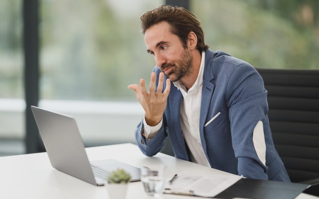 Man looking at laptop, hand gesturing as if he's on a video call talking to someone else